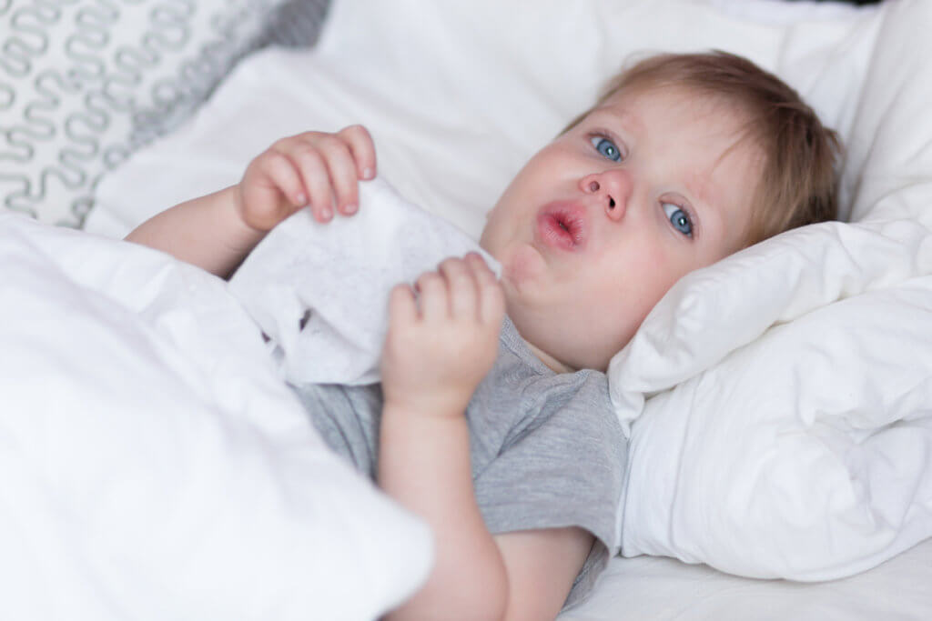 Bebé acostado en la cama y tosiendo