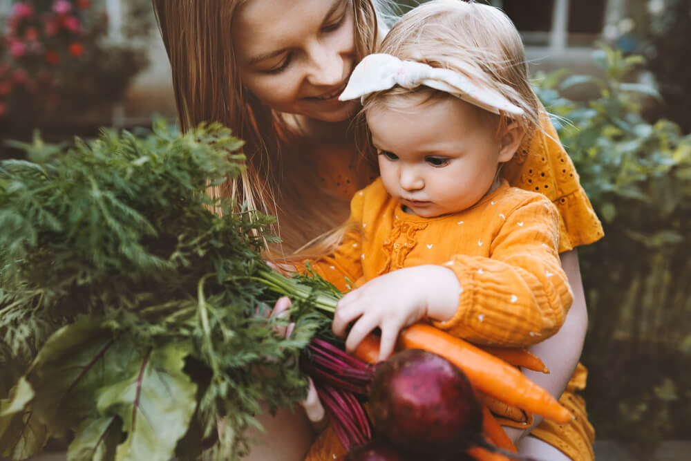 Mamá ofrece hortalizas frescas a bebé para que pueda tocarlas