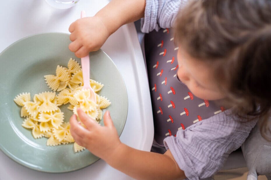 Bebé comiendo lazos de pasta con cuchara