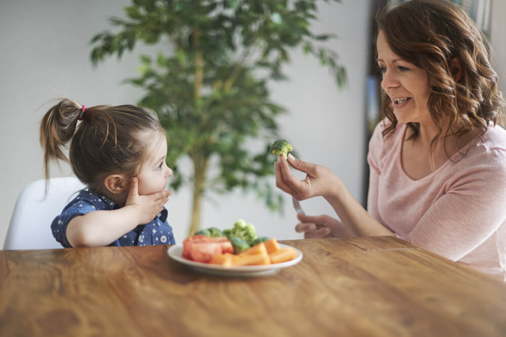 Mamá ofrece verduras a niña pequeña