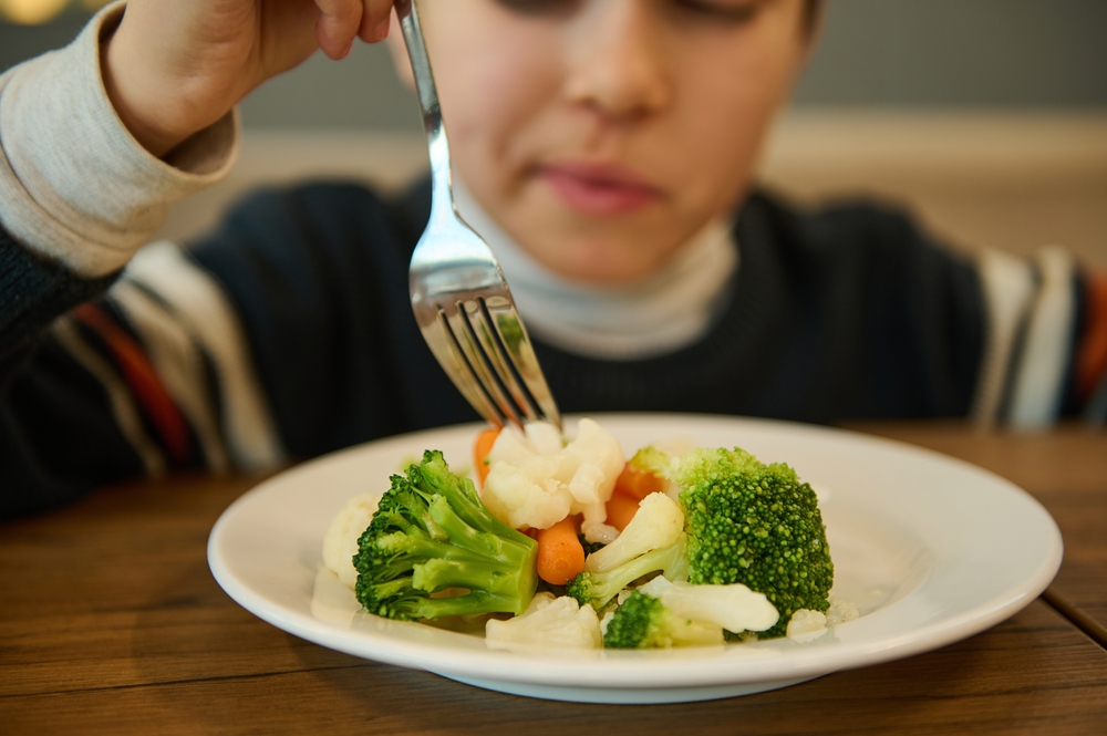 Niña comiendo un plato de verduras al vapor con brócoli, coliflor y zanahoria